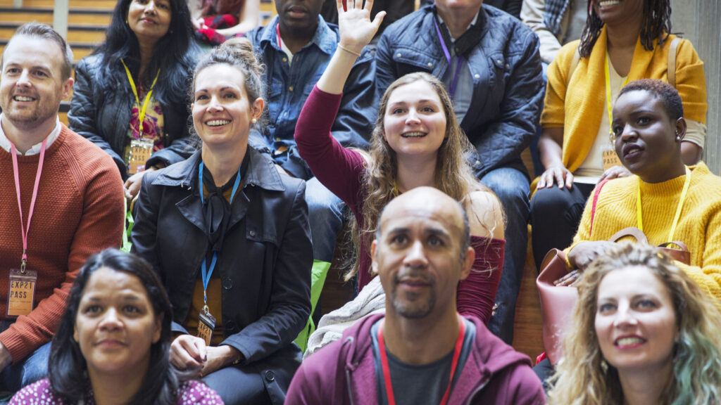 Person with hand raised sitting in an audience with other people