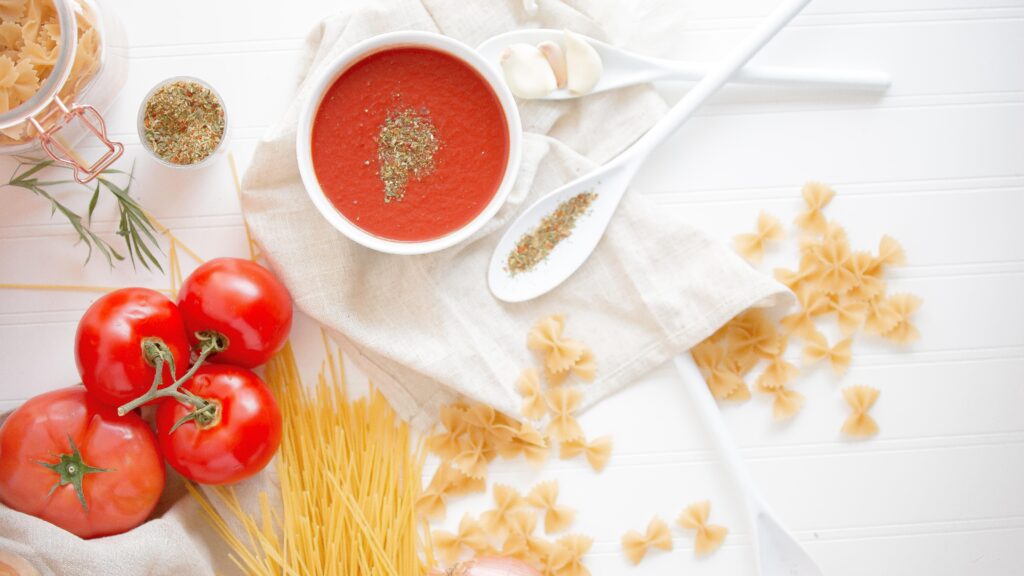 top down photograph of ingredients on a table - tomatoes, onions, pasta, spices